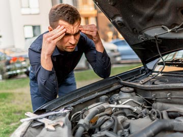 Eine Person inspiziert einen Auto-Motor mit konzentriertem Gesichtsausdruck, umgeben von Werkzeugen, in einer äußeren Umgebung.